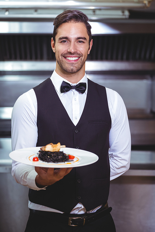 Handsome waiter holding a plate of squid ink spaghetti in the restaurant kitchen
