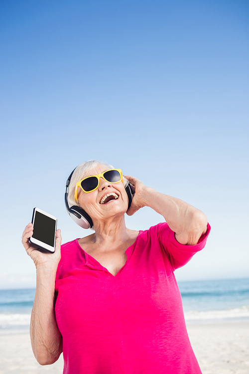 Senior woman listening music with headphone on the beach