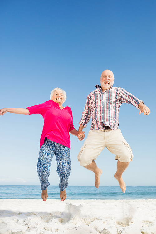 Happy senior couple jumping on the beach