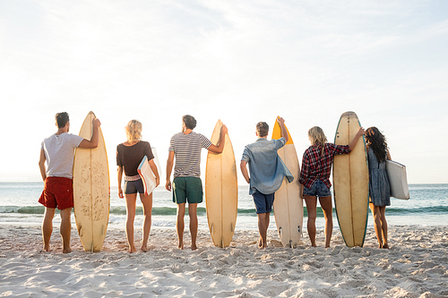 Happy friends standing in line with surfboards on the beach