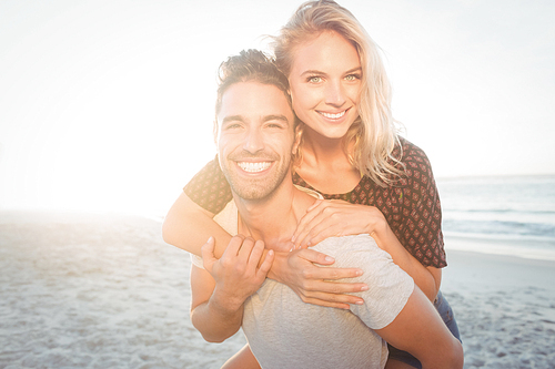 Portrait of a young man piggybacking beautiful woman on the beach