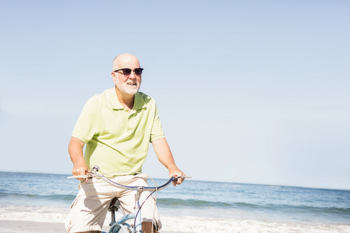 Smiling senior man riding bike on the beach