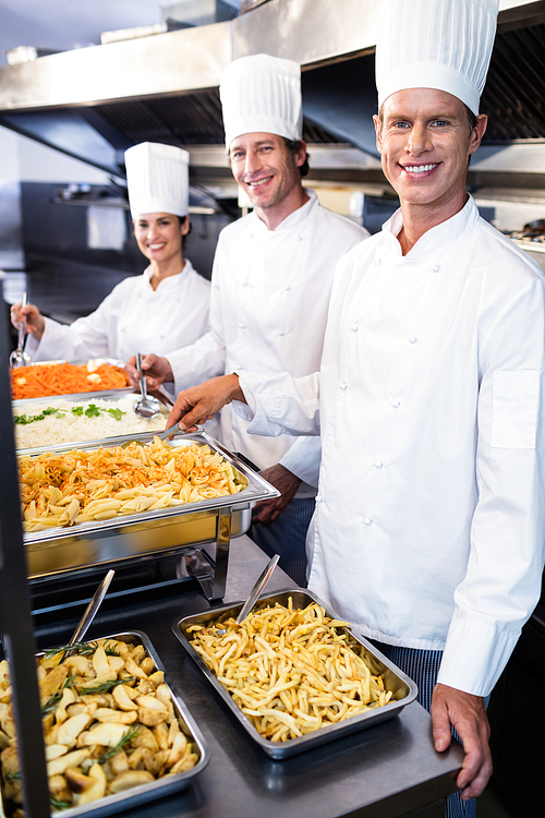 Portrait of chefs standing at serving trays of pasta in commercial kitchen