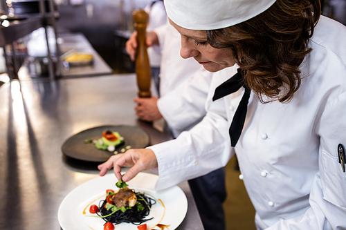 Female chef garnishing meal on counter in commercial kitchen