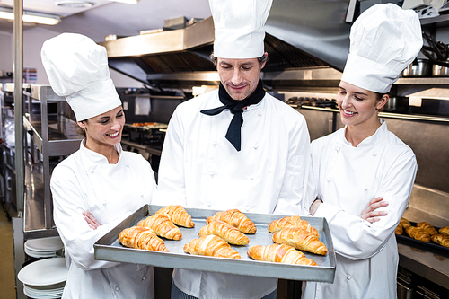 Three chefs in kitchen holding a tray of baked croissant in commercial kitchen