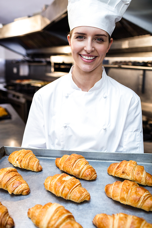 Portrait of a chef holding tray of croissants in commercial kitchen