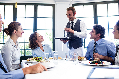 Waiter serving water to the business people in restaurant