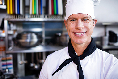 Portrait of smiling chef in commercial kitchen and thee chefs cooking in background