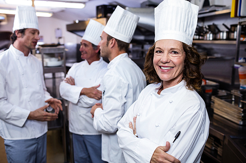 Portrait of smiling chef in commercial kitchen and thee chefs discussing In background