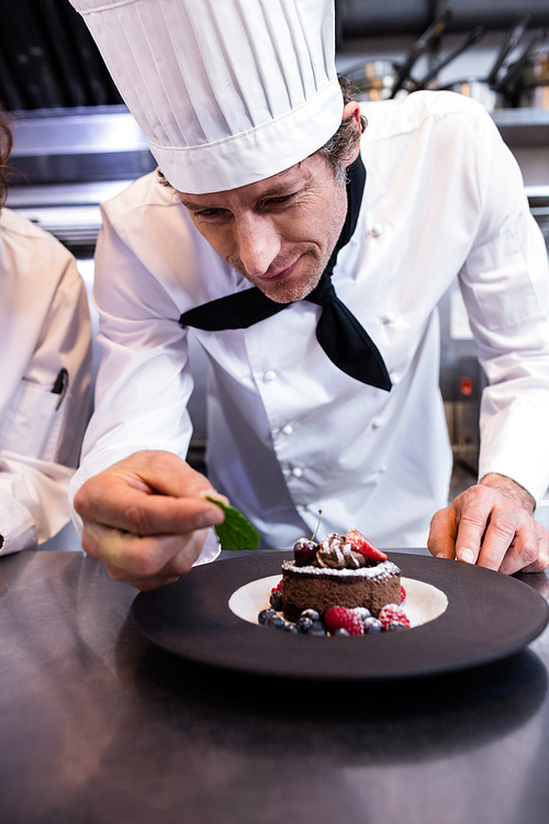 Male chef garnishing dessert with a mint leaf in commercial kitchen