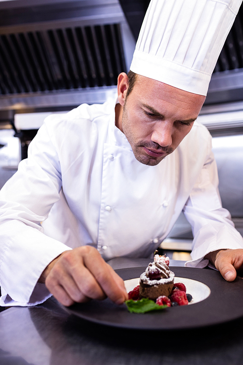 Male chef garnishing dessert plate in commercial kitchen