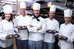 Happy chefs presenting their dessert plates in commercial kitchen