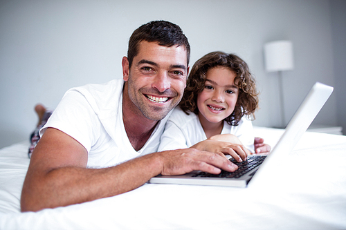 Portrait of father and son using laptop on bed in bedroom