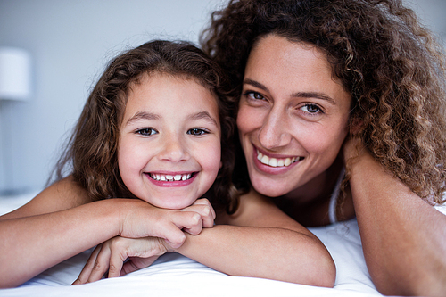 Portrait of mother and daughter embracing on bed in bedroom