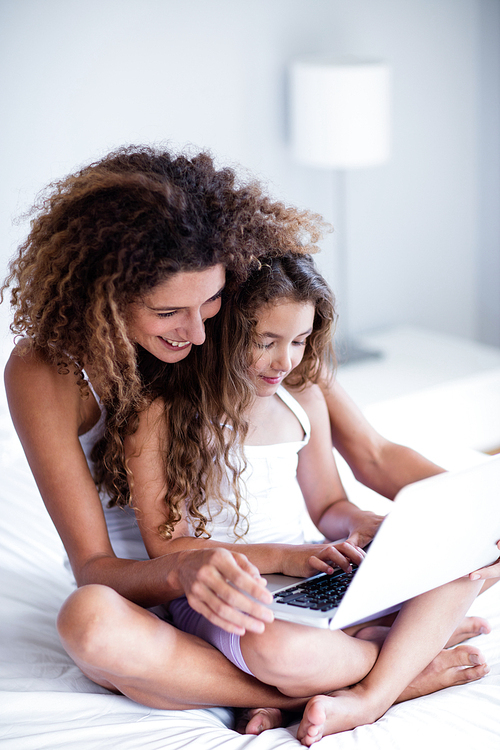 Mother and daughter using laptop on bed in bedroom