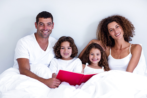 Portrait of family reading book together on bed in bedroom