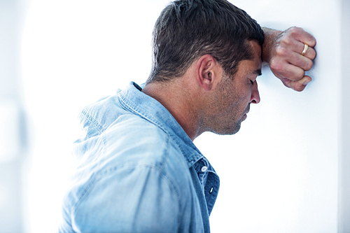 Close-up of upset man leaning on wall with hand on forehead