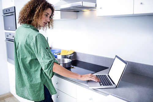 Woman working on laptop while cooking in kitchen