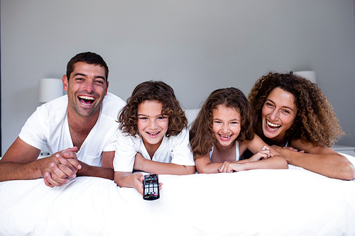 Portrait of happy family lying on bed and watching television