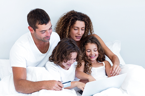 Family with credit card shopping online on bed in bedroom