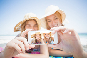 Two happy friends taking selfie while lying on the beach