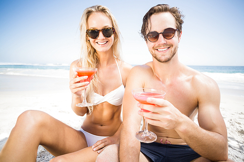 Portarit of happy young couple sitting on the beach and having cocktail glasses