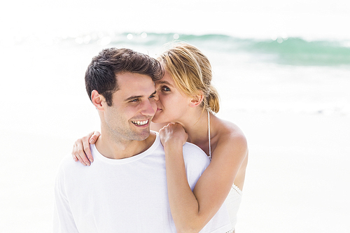 Young woman whispering in mans ears on the beach on a sunny day