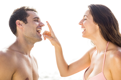 Happy woman applying moisturizer on mans nose at the beach