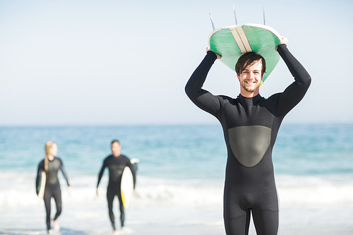 Happy man in wetsuit carrying surfboard over head on the beach