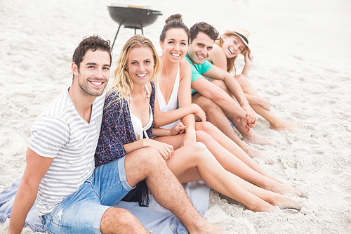 Group of happy friends sitting side by side on the beach
