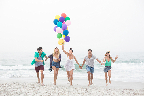 Group of happy friends running on the beach with multicolored balloons