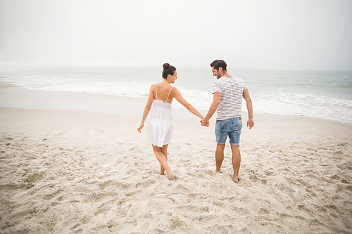 Rear view of couple holding hands and walking on the beach on a sunny day