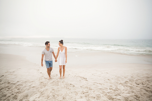 Happy couple holding hands and walking on the beach on a sunny day