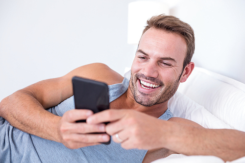 Young man lying on bed using mobile in his bedroom