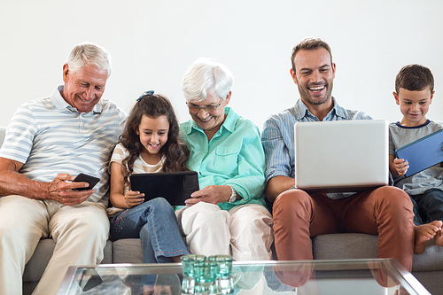 Happy family sitting on sofa using a laptop, digital, tablet, mobile phone in living room