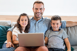 Portrait of father sitting on sofa with son and daughter