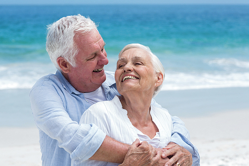 Senior couple embracing with arms around at the beach