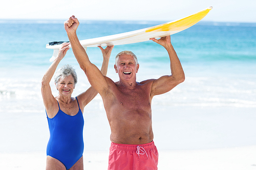 Cute mature couple holding a surfboard over their heads on the beach