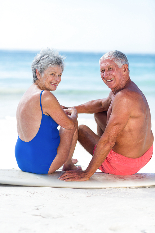 Cute mature couple sitting on a surfboard on the beach