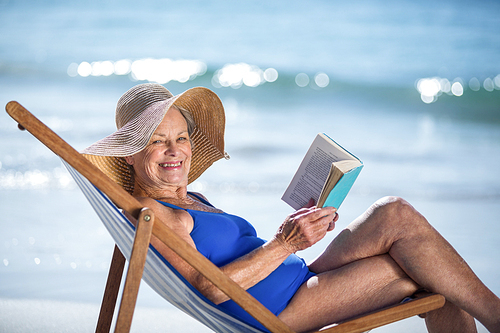 Pretty mature woman reading a book lying on deck chair on the beach