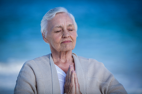 Senior woman relaxing with joined hands on the beach