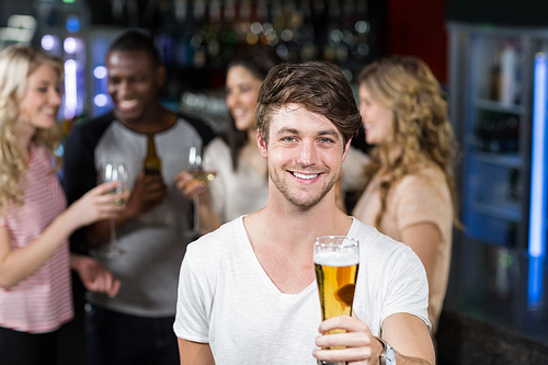 Smiling man showing a beer with his friends in a nightclub