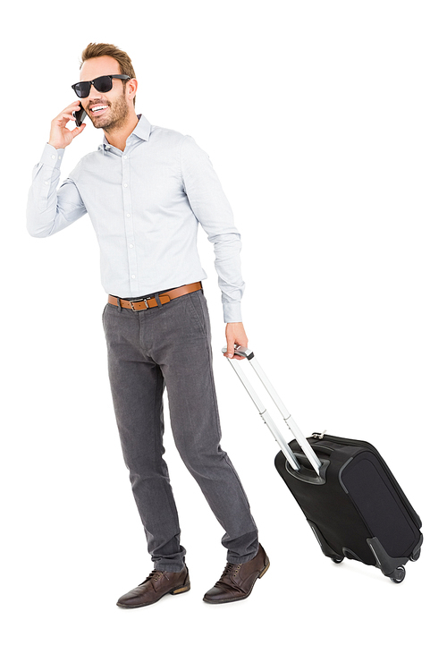 Young man holding trolley bag and talking on mobile phone on white background