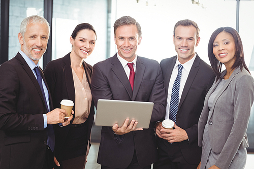 Portrait of businesspeople standing together with a laptop in office