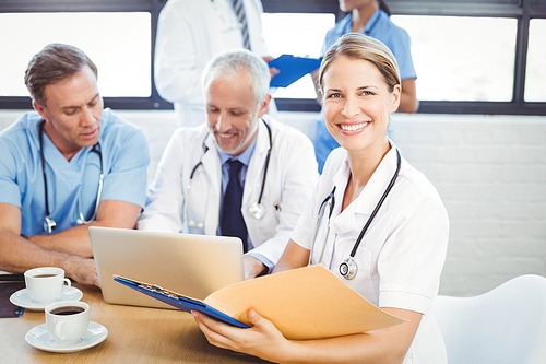 Female doctor holding a medical report in conference room and colleagues using laptop