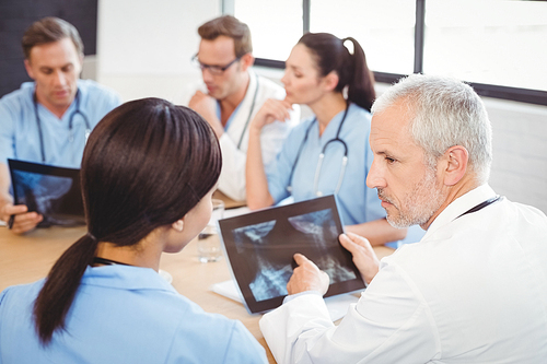 Doctors examining an x-ray report in hospital and colleagues discussing in background