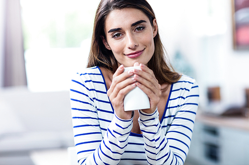 Close-up portrait of beautiful young woman holding mug at home