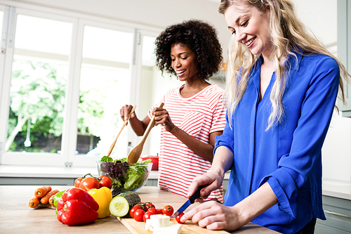Cheerful female friends preparing food at table in kitchen