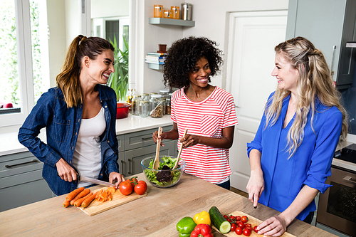 Young female friends smiling while preparing food in kitchen at home