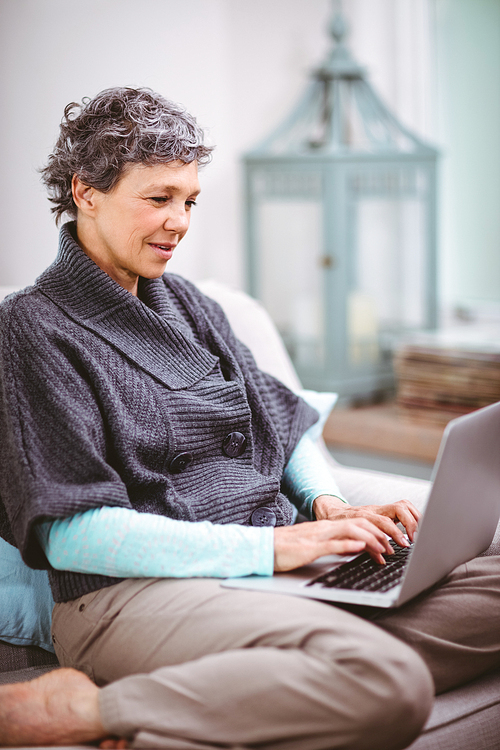 Mature woman using laptop while sitting on sofa at home